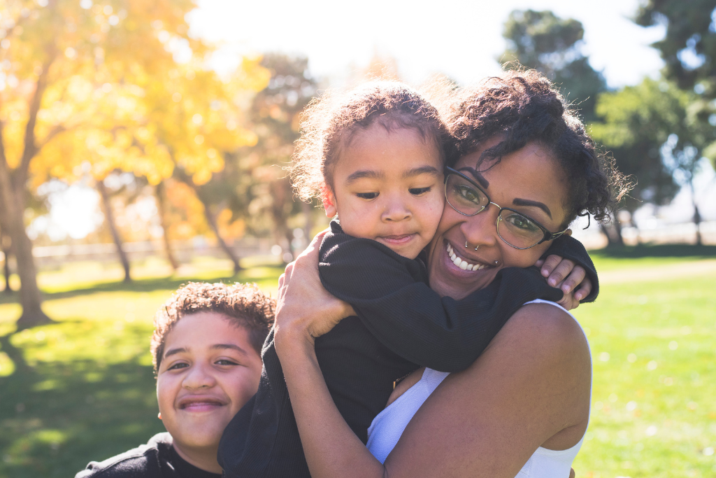 A young mom holding one of her two kids and smiling