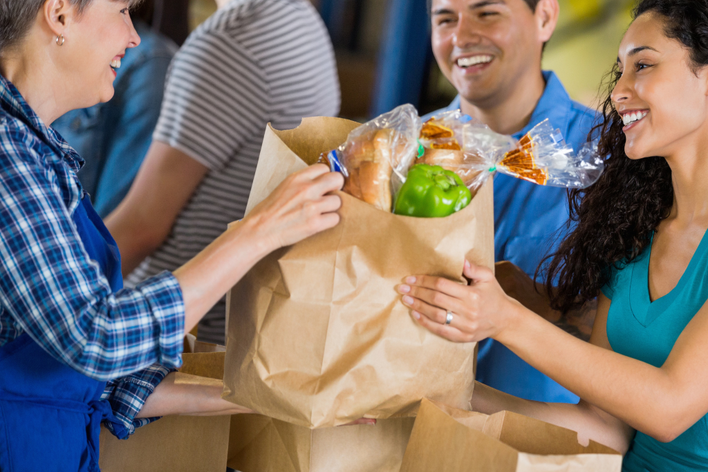 Volunteer handing a bag of groceries to a young smiling couple